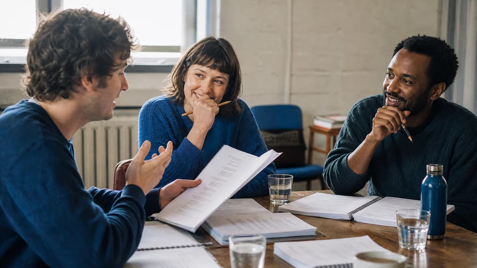 A screenwriter and two actors sharing a lively table read around cleanly formatted screenplay pages